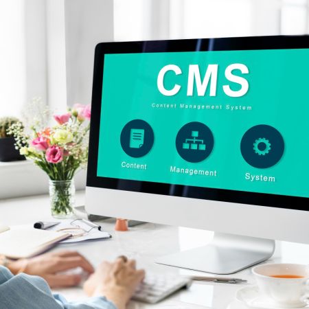 man sat a desk typing on a computer, there is a bunch of flowers and the screen says CMS